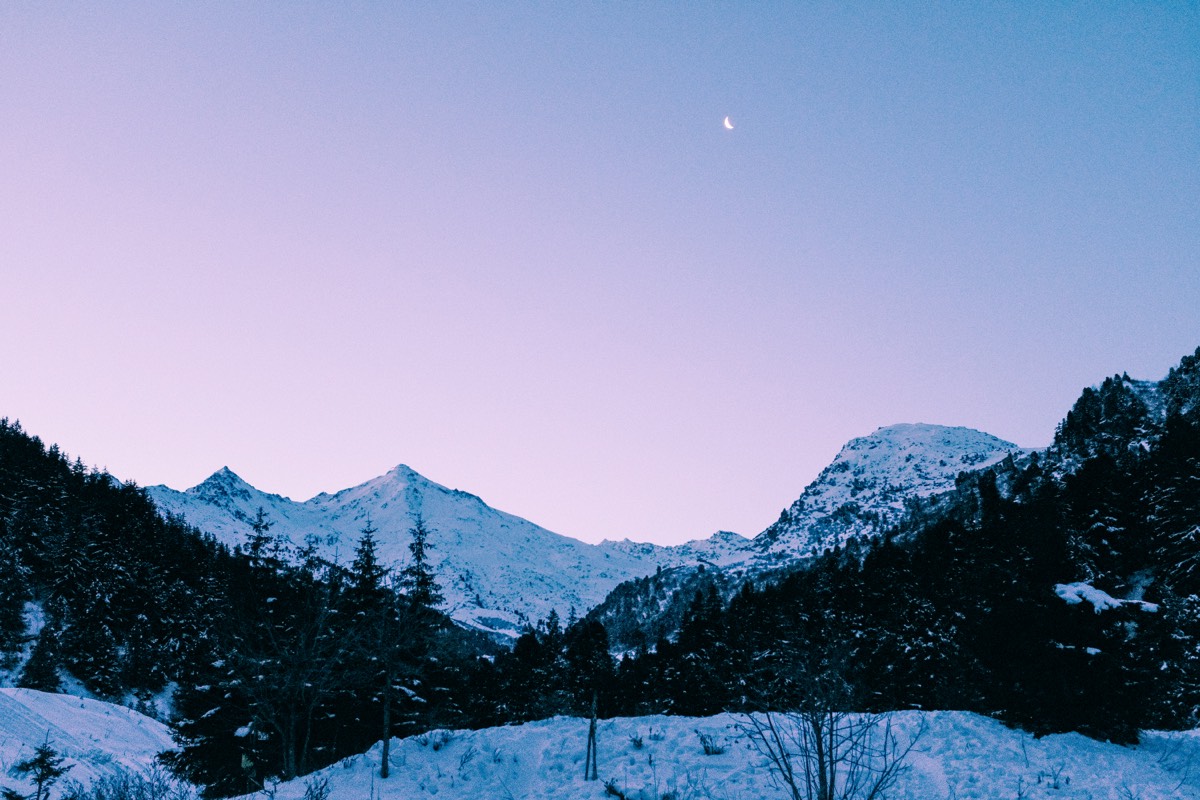Snow covered alpine peaks at dusk under a crescent moon, in the Trois Vallées