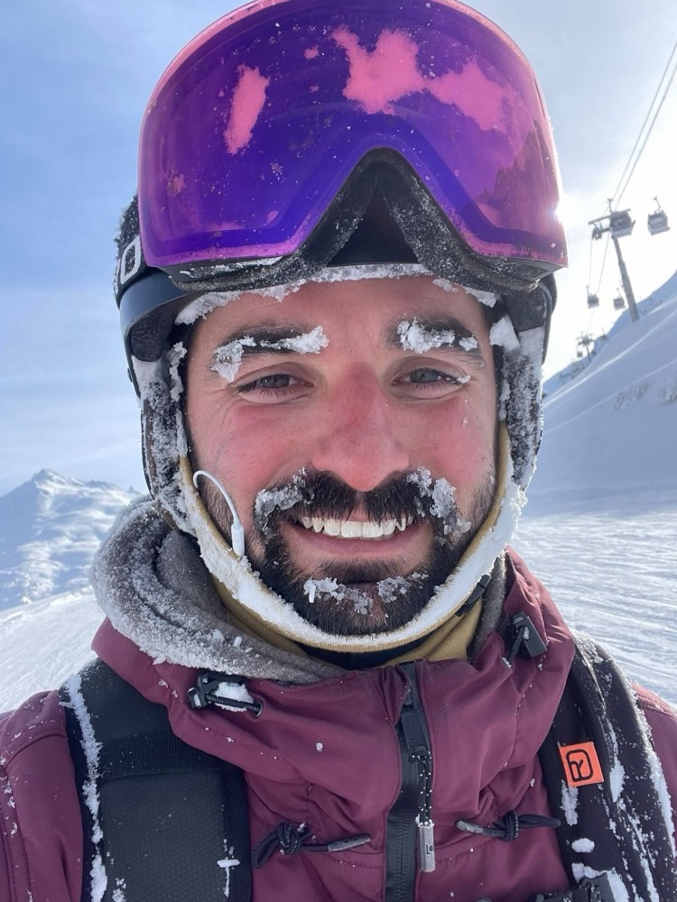 Zack on the mountain in ski gear, smiling with snow on his beard